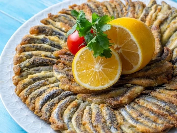 Limon dilimleri ve maydanozla servis edilen çıtır hamsi tava