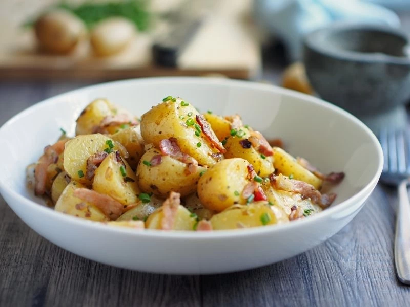 Beyaz kasede yeşilliklerle harmanlanmış patates salatası