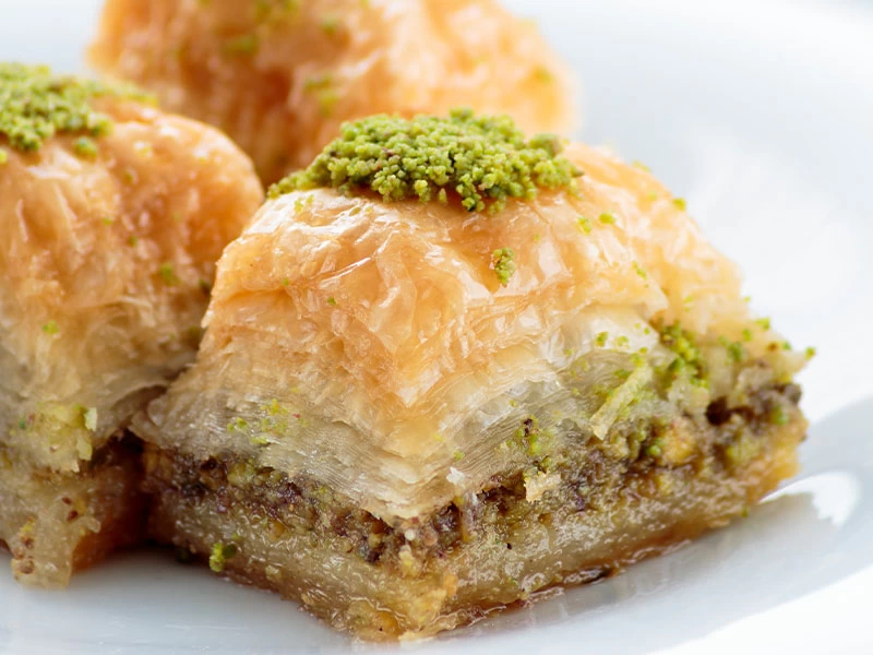 Üzeri yeşil tozla süslenmiş, iç katmanları görünen baklava dilimi