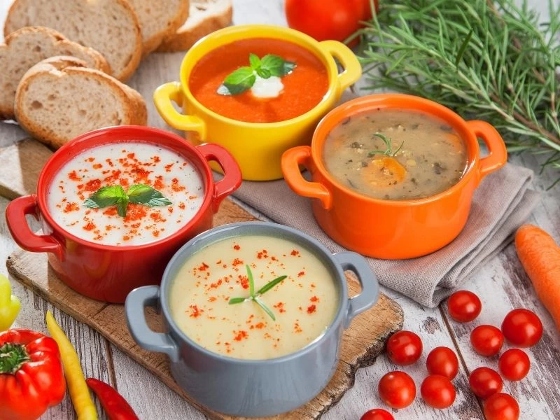 Ekmek ve sebzelerle birlikte servis edilen farklı çorbalar