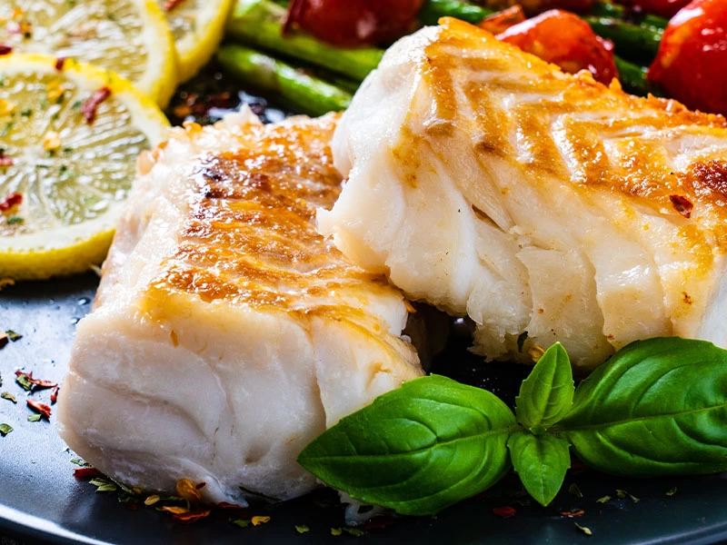 Limon dilimleri ve yeşillikler yanında servis edilen pişmiş balık filetosu