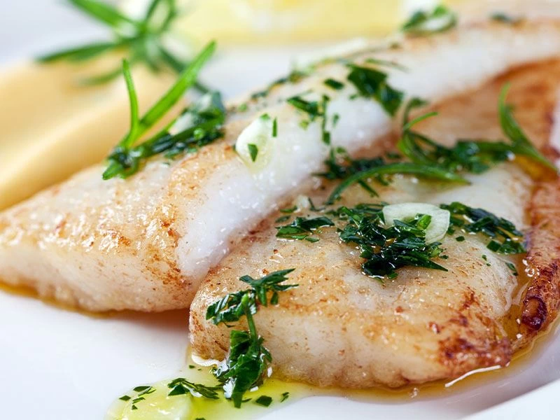 Zeytinyağı ve yeşilliklerle servis edilen pişmiş balık parçaları