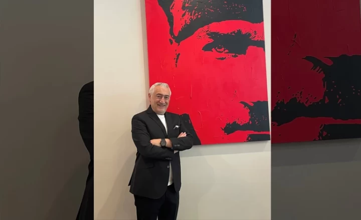 Bilge Özdemir, kırmızı ve siyah tonlarda bir Atatürk portresinin önünde duruyor