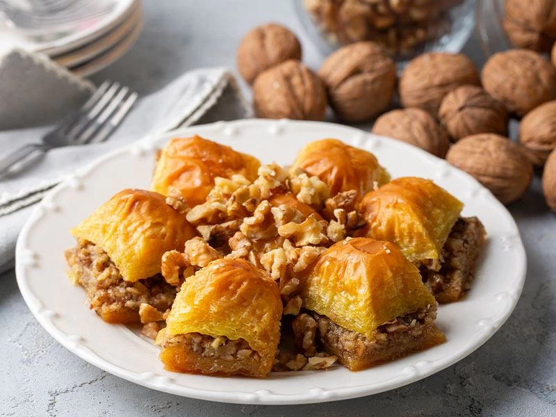 Tabakta cevizli baklava dilimleri ve arka planda kabuklu cevizler