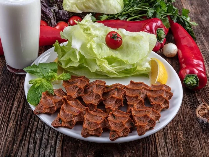 Marul, biber ve limonla servis edilen koyu kırmızı çiğ köfte