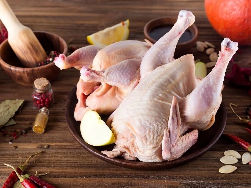 Baharat ve limon eşliğinde tabakta duran çiğ bütün tavuk