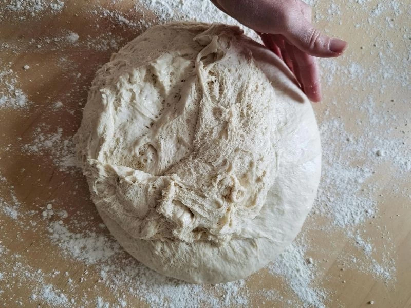 Un serpilmiş tezgâhta cıvık ekmek hamurunu yoğuran bir el