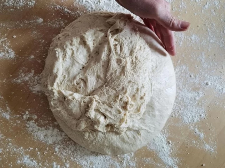 Un serpilmiş tezgâhta cıvık ekmek hamurunu yoğuran bir el