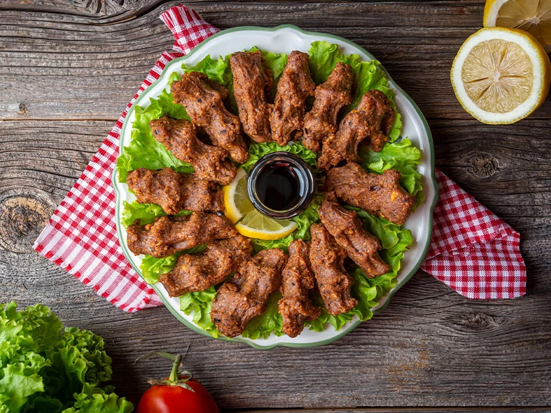 Düzenli Çiğ Köfte Sunumu Yeşilliklerle çevrili tabakta düzenli dizilmiş çiğ köfteler