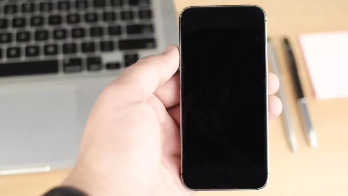 Bilgisayar ve kalemlerin yanında elde tutulan ekranı kapalı akıllı telefon