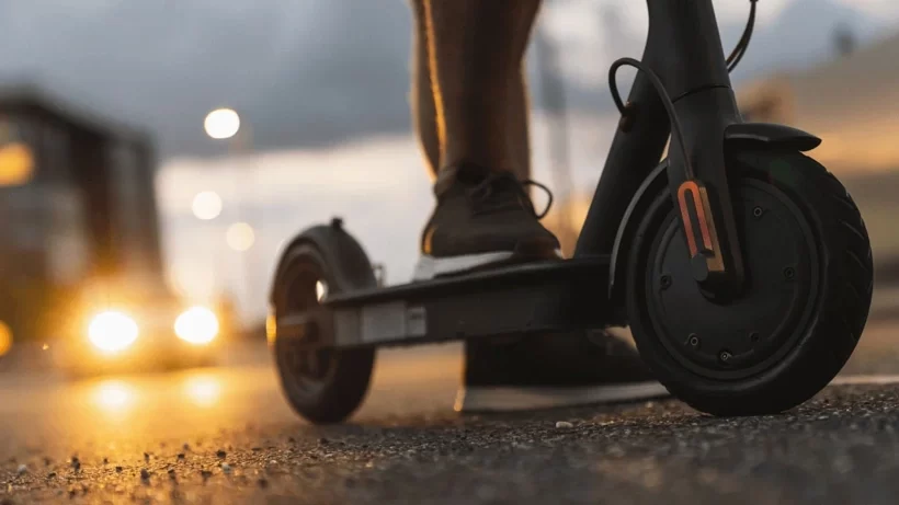 Elektrikli scooter’ın tekerleği ve üzerinde duran bir kişinin ayakları yakın planda görülüyor.