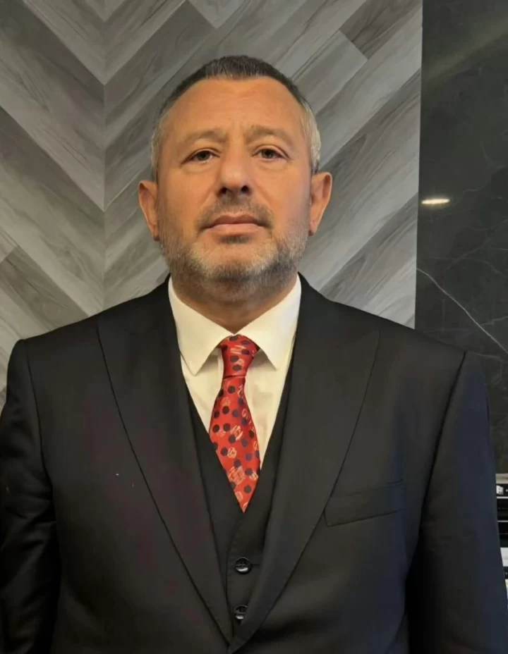 Erdal Cevahir, siyah takım elbise ve kırmızı kravatla kameraya bakıyor