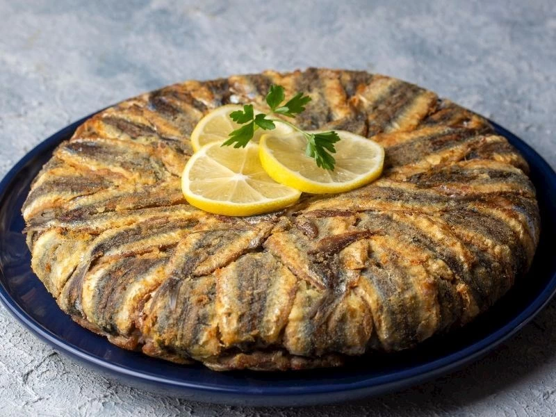 Limon dilimleri ve maydanozla süslenmiş, hamsilerle kaplı hamsili pilav