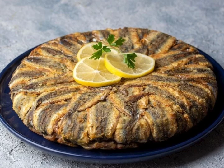 Limon dilimleri ve maydanozla süslenmiş, hamsilerle kaplı hamsili pilav