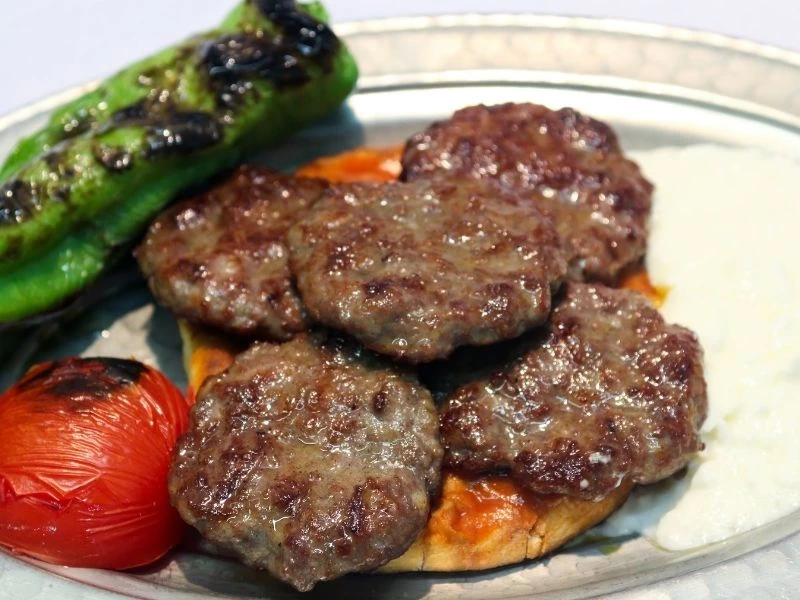 Izgara köfteler, közlenmiş domates ve biberle servis ediliyor