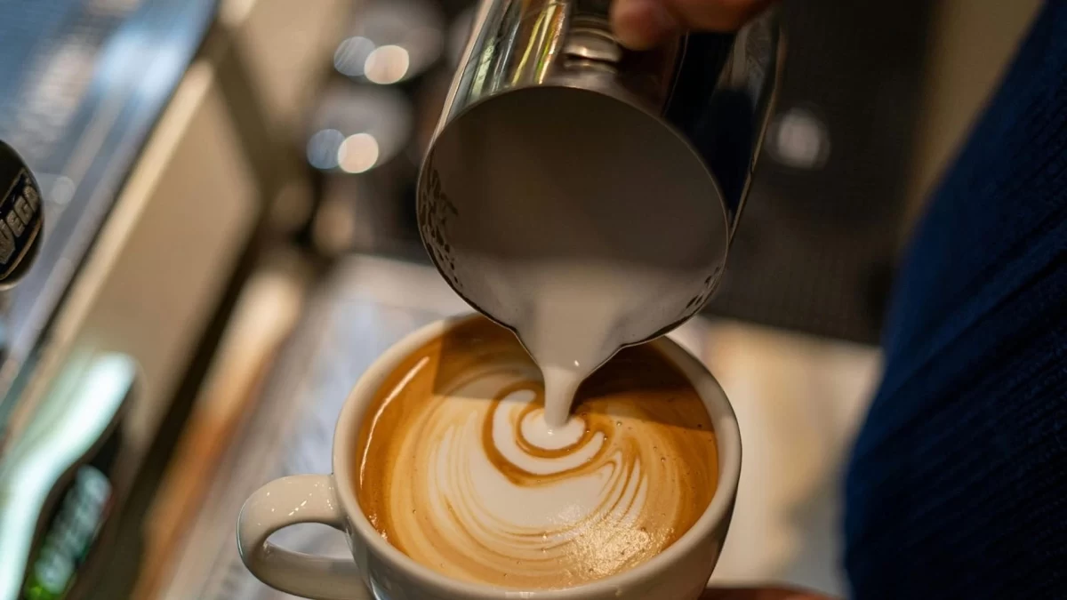 Bir fincana süt dökülerek kahve üzerine latte sanatı yapılıyor.