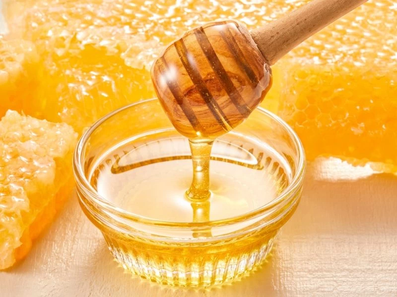 Cam kasedeki bala ahşap kaşıktan bal akıyor