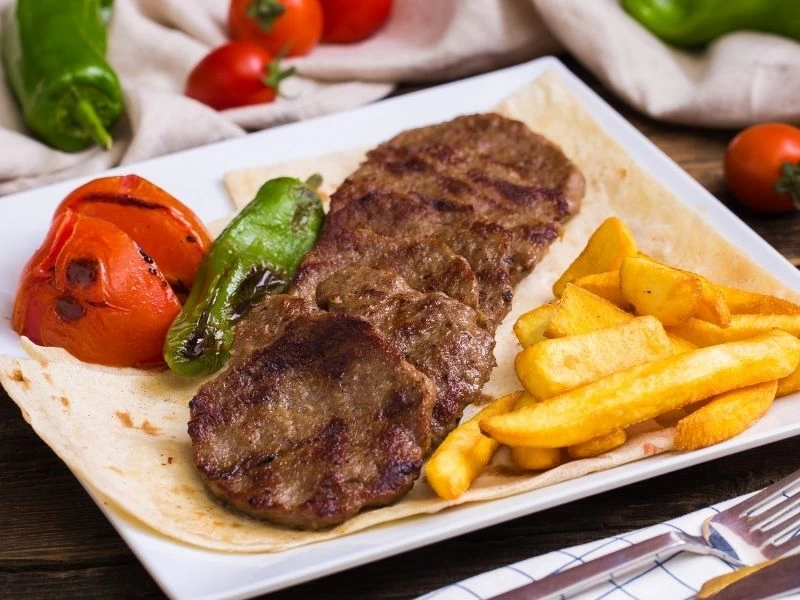 Közlenmiş domates ve biberle servis edilen köfteler, yanında patates kızartması
