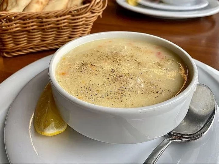 Beyaz kasede, yanında limon dilimi bulunan tavuk çorbası