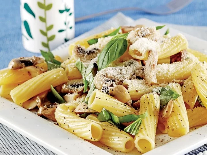 Üzerinde parmesan ve fesleğen bulunan mantarlı makarna