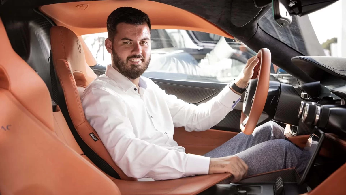 Mate Rimac, otomobilin turuncu deri koltuğunda otururken direksiyonu tutuyor.