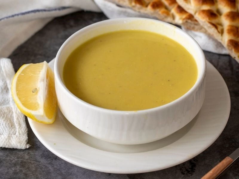 Beyaz kâsede mercimek çorbası ve yanında limon dilimi