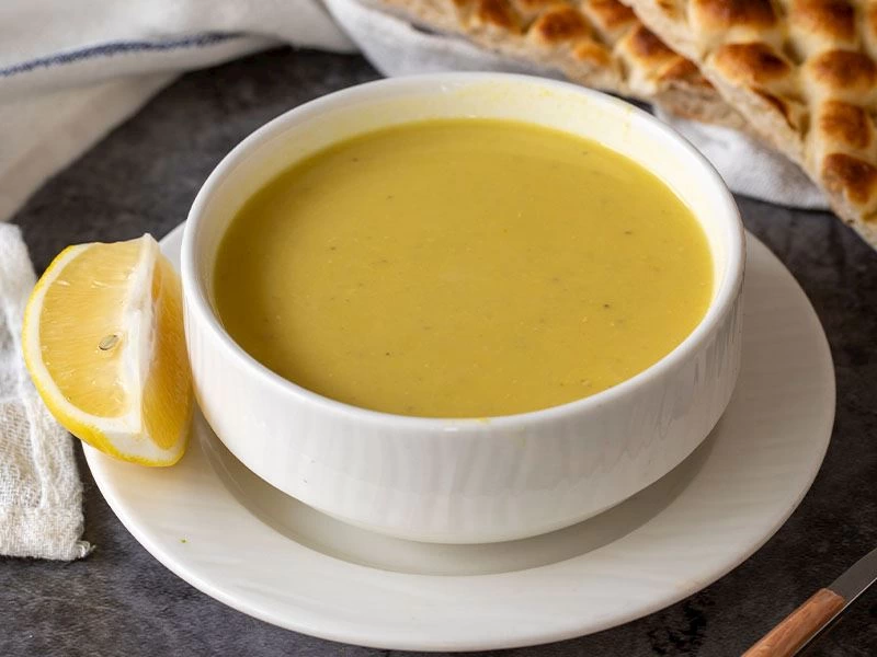 Beyaz kâsede limon ve ekmekle servis edilen mercimek çorbası