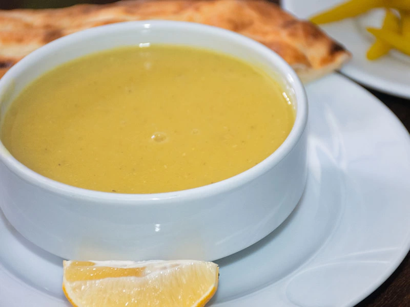 Beyaz kâsede pürüzsüz mercimek çorbası ve limon dilimi