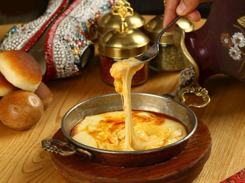 Kaşıkla alınan mıhlama, masada ekmek ve baharatlıklarla birlikte