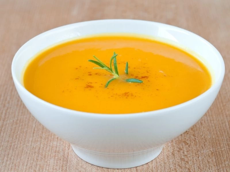 Beyaz kasede, üzerine yeşil ot eklenmiş pürüzsüz turuncu çorba