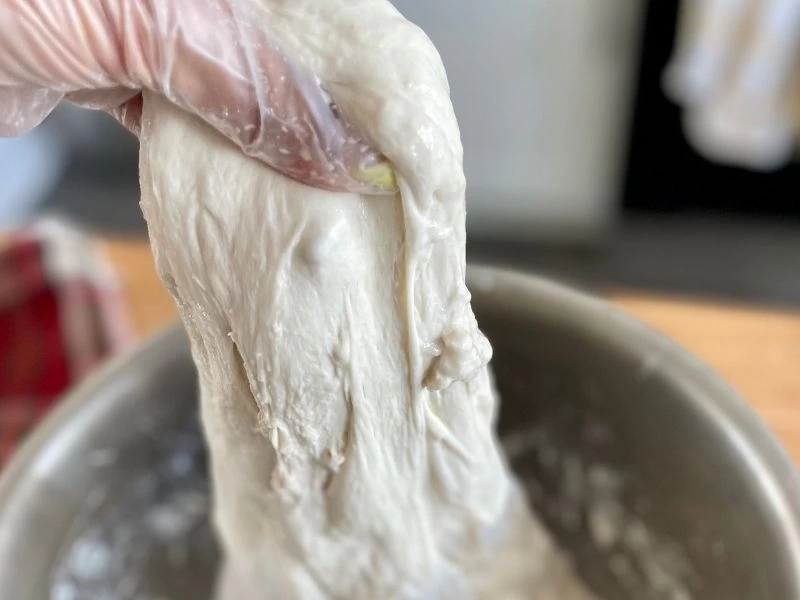 Eldivenli el, metal bir kabın içindeki esnek hamuru yukarı doğru kaldırıyor