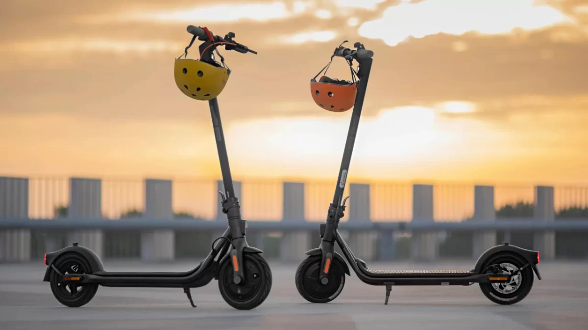 Şehirde kaldırım boyunca elektrikli scooter kullanan kişiler ve park edilmiş kiralık scooter’lar.