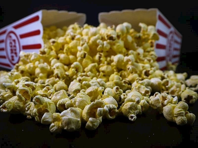 Koyu zemin üzerinde dağılmış patlamış mısır ve arkada sinema tipi mısır kutuları