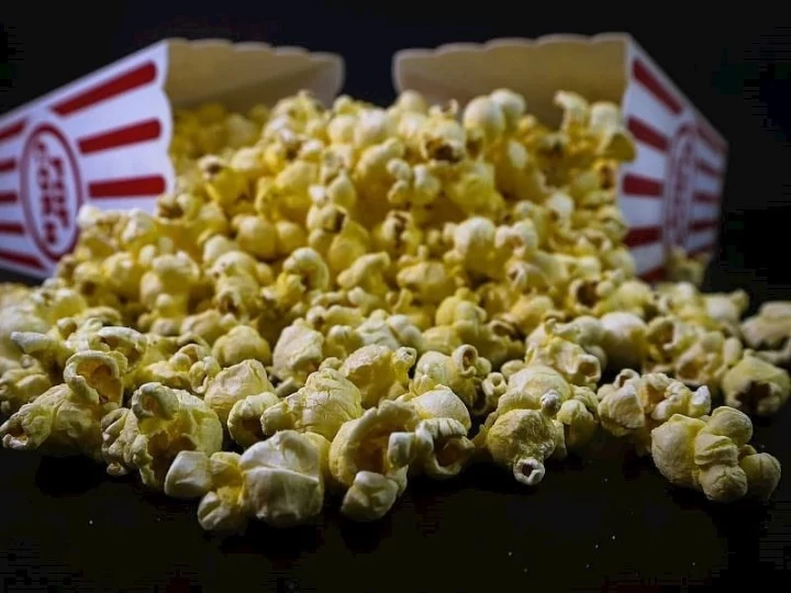 Koyu zemin üzerinde dağılmış patlamış mısır ve arkada sinema tipi mısır kutuları