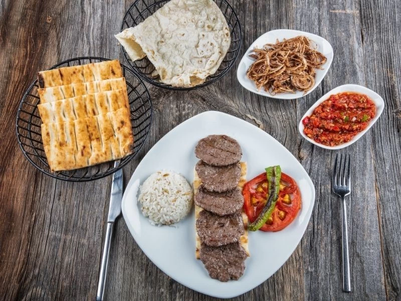 Pide üzerinde servis edilen Sivas köftesi; yanında pilav, domates ve közlenmiş biber