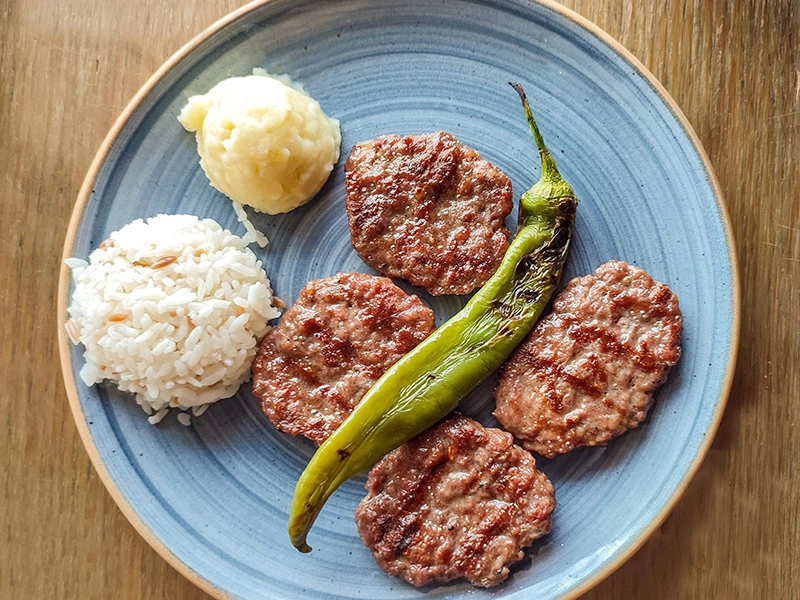 Mavi tabakta köfte, pilav, patates püresi ve közlenmiş biber