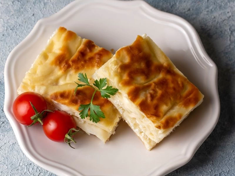 Beyaz tabakta domates ve maydanozla sunulan kızarmış su böreği dilimleri