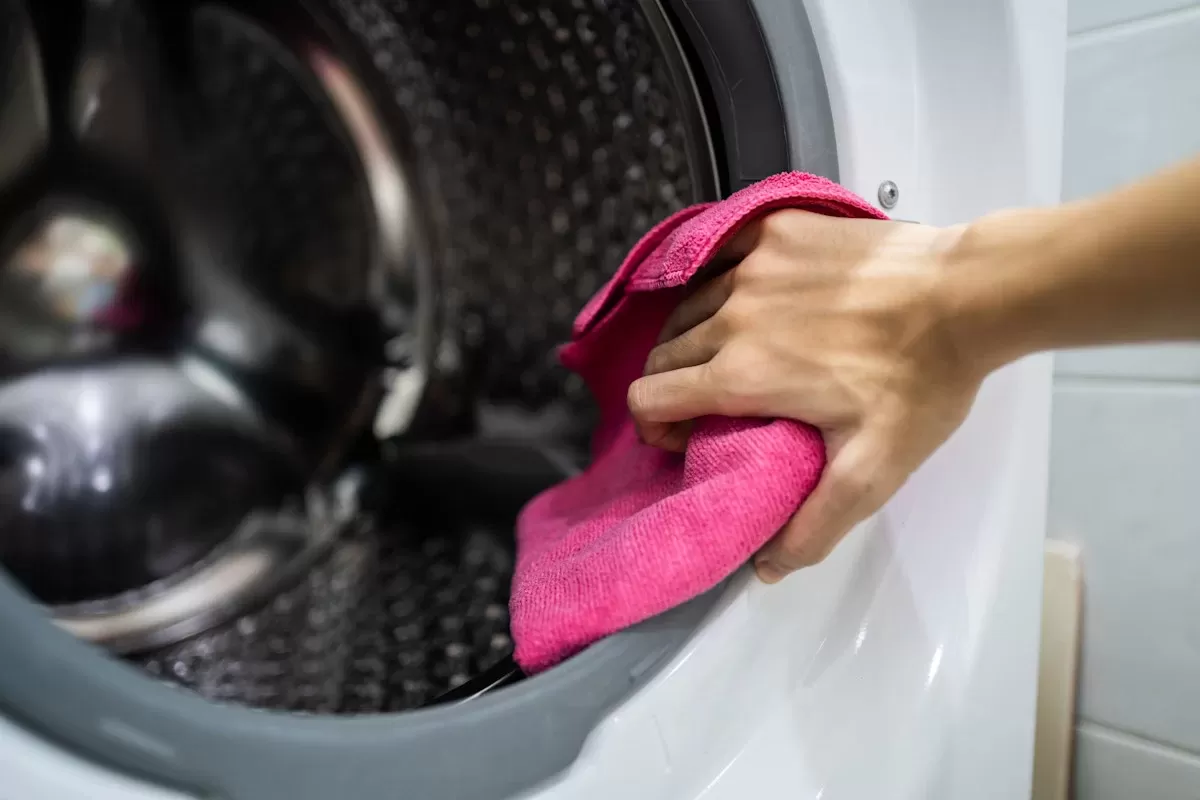 Çamaşır makinesinin tamburunu pembe bezle silen bir el