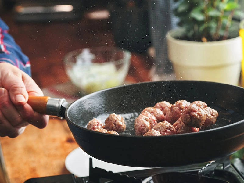 Tavada pişen köfteler ve tavayı tutan el