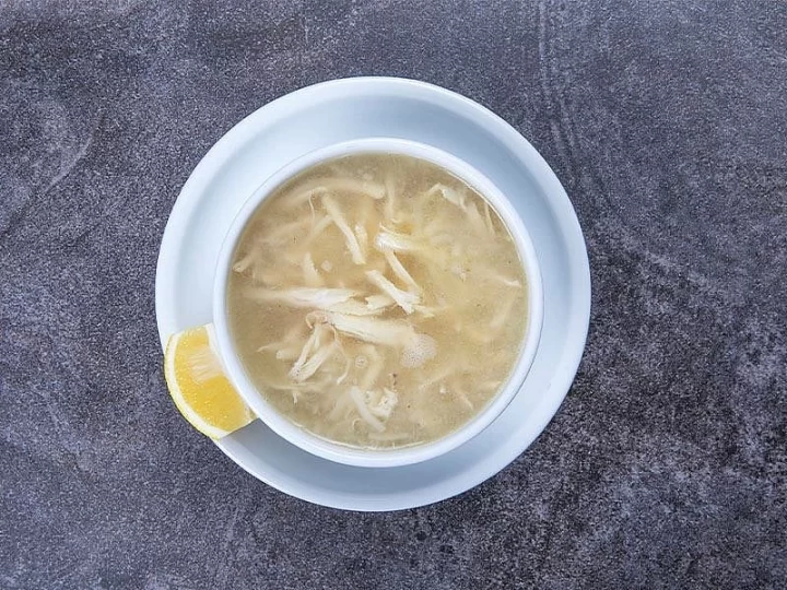 Beyaz kâsede tavuk suyu çorbası ve yanında limon dilimi