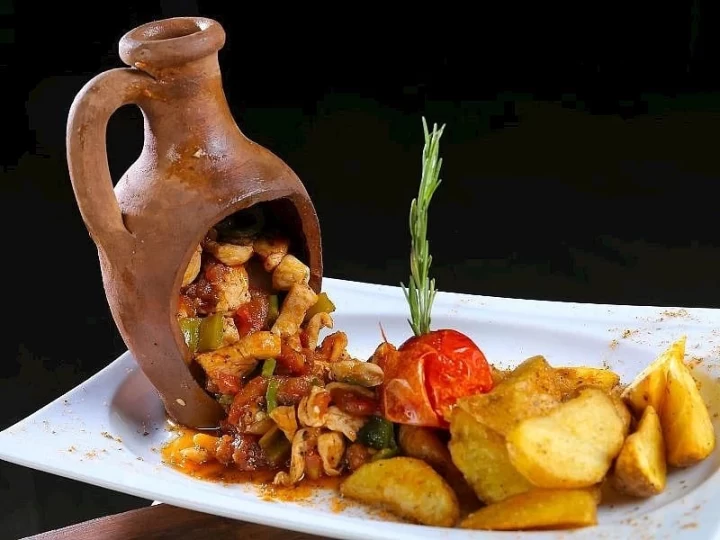 Toprak testi içinde pişmiş kebap, tabakta patates ve domatesle servis ediliyor