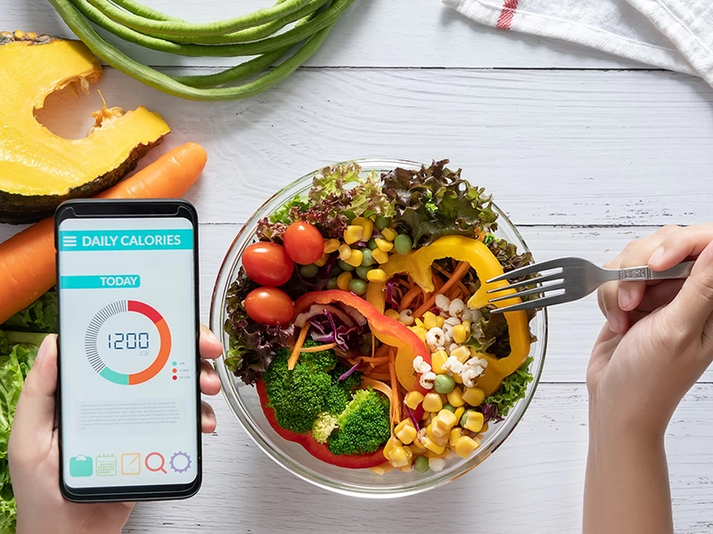 Salata yerken kullanılan çatal ve günlük kalori bilgisi gösteren telefon ekranı