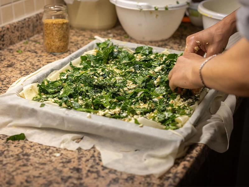 Tepsideki yufkanın üzerine yayılan yeşillikli börek harcı