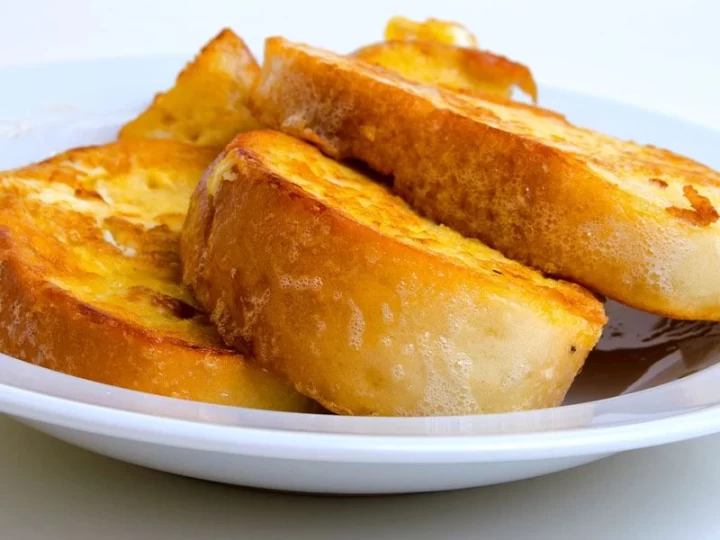 Beyaz tabakta üst üste dizilmiş kızarmış yumurtalı ekmek dilimleri