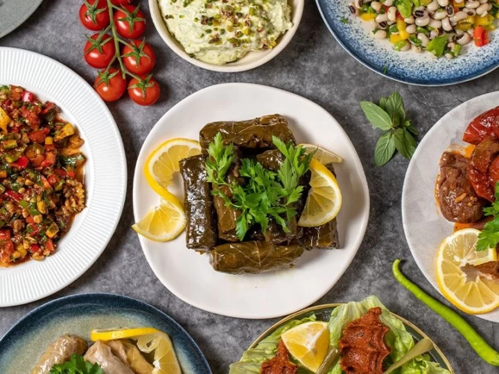 Ortada limon ve yeşilliklerle sunulan sarma, çevresinde çeşitli zeytinyağlı yemekler